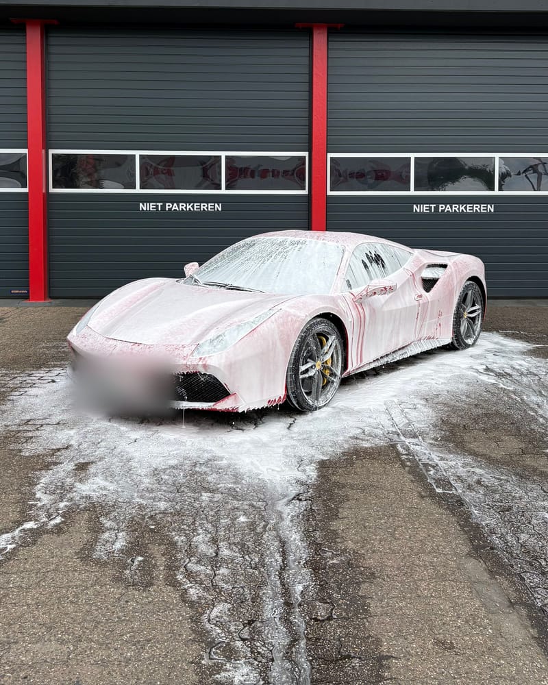 De rode Ferrari helemaal ingeschuimd met snow foam, voor een donkere garagedeur