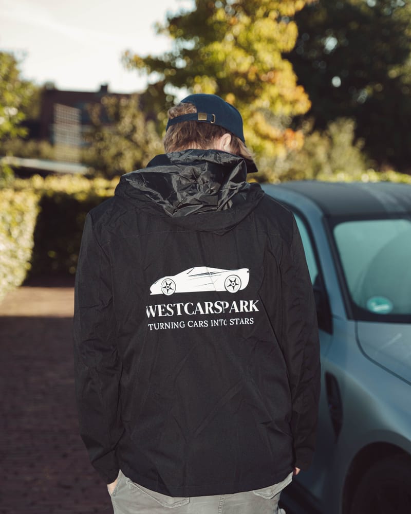Ruben van achteren gezien, in een zwarte WestCarSpark-jas met logo en slogan