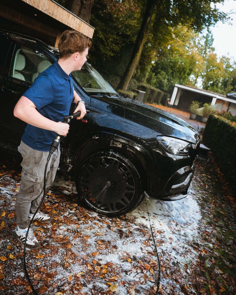 Ruben spuit een zwarte Maybach af met de hogedrukreiniger op een oprit vol herfstbladeren