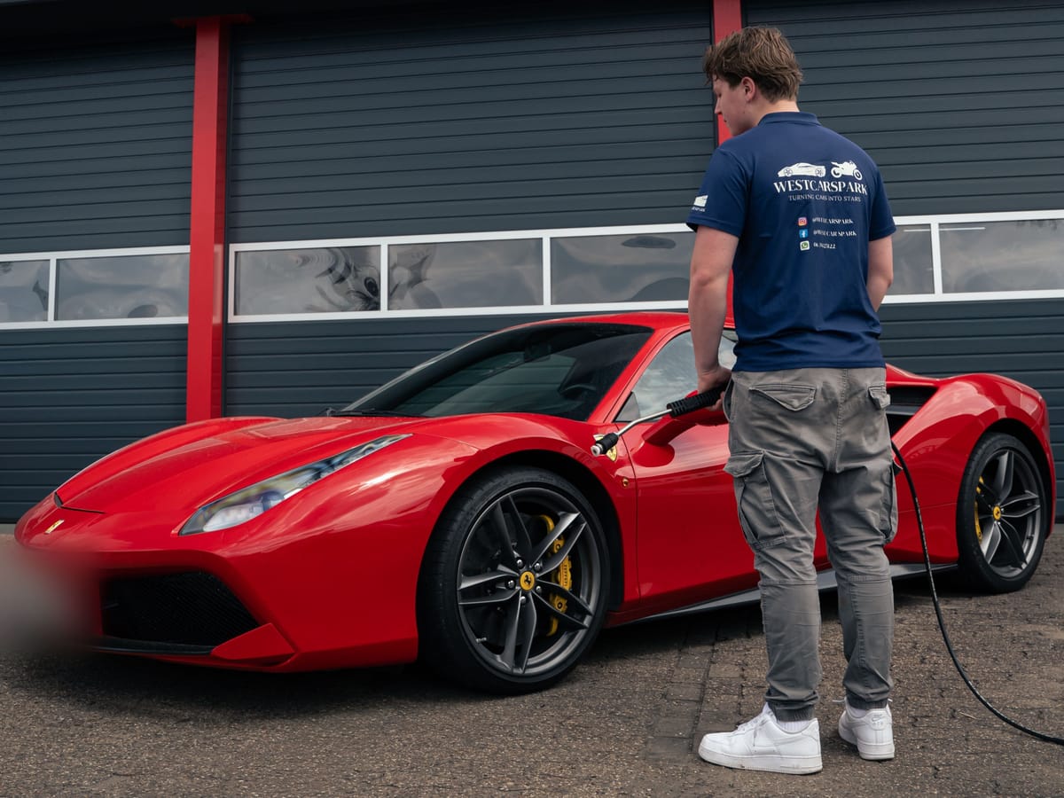Ruben in een WestCarSpark-polo met de hogedrukreiniger naast een rode Ferrari 488 GTB