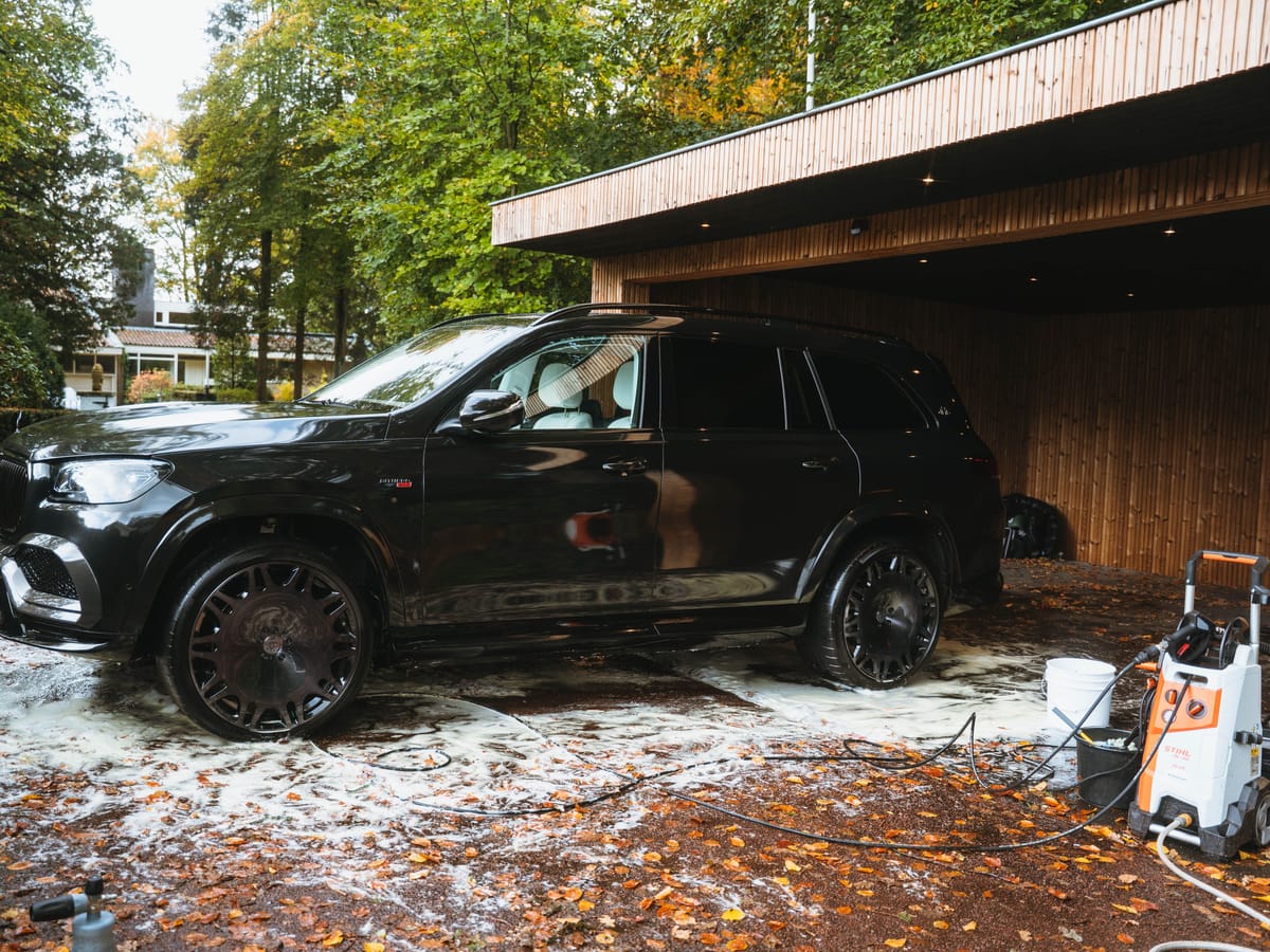 Zwarte Maybach Brabus 800, glanzend nat onder een carport, met de hogedrukreiniger ernaast